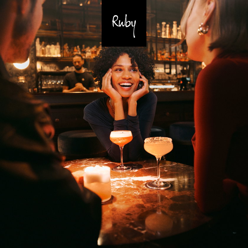 People chat around a table in a bar, with cocktails in front of them.