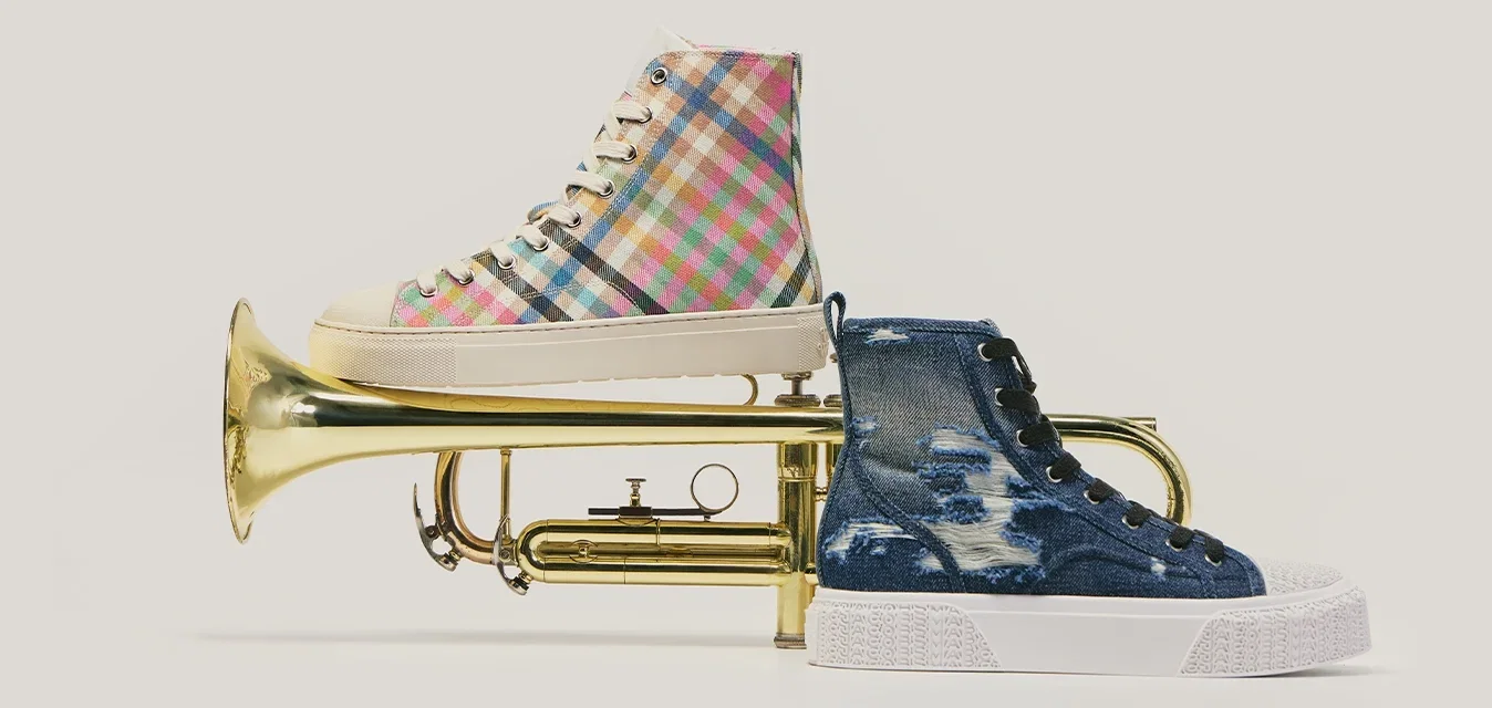 Trombón de latón con una zapatilla azul en la boquilla y una zapatilla de cuadros multicolores equilibrada en la campana.