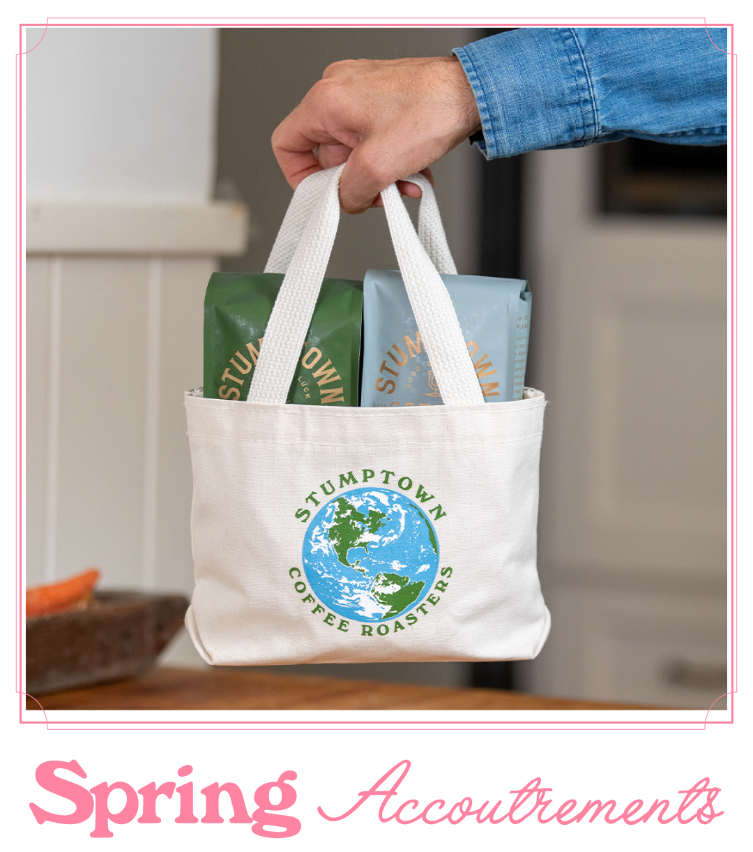 Hand holding a Stumptown Coffee Roasters mini canvas tote with a globe logo, filled with two coffee bags, with the headline “Spring Accoutrements” below.