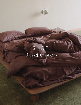 Dark purple sheets on a wooden bed frame with green carpet