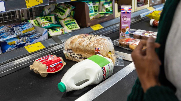 Eggs, bread, milk, and other food on a conveyor belt. Blurred in the foreground is the hand of a shopper.