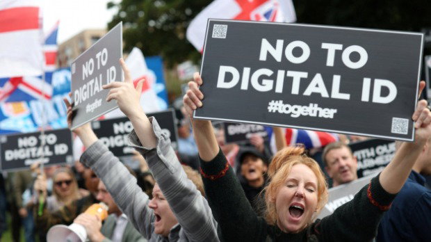 A woman in a crowd holds a black sign which reads 'NO TO DIGITAL ID' in white lettering.