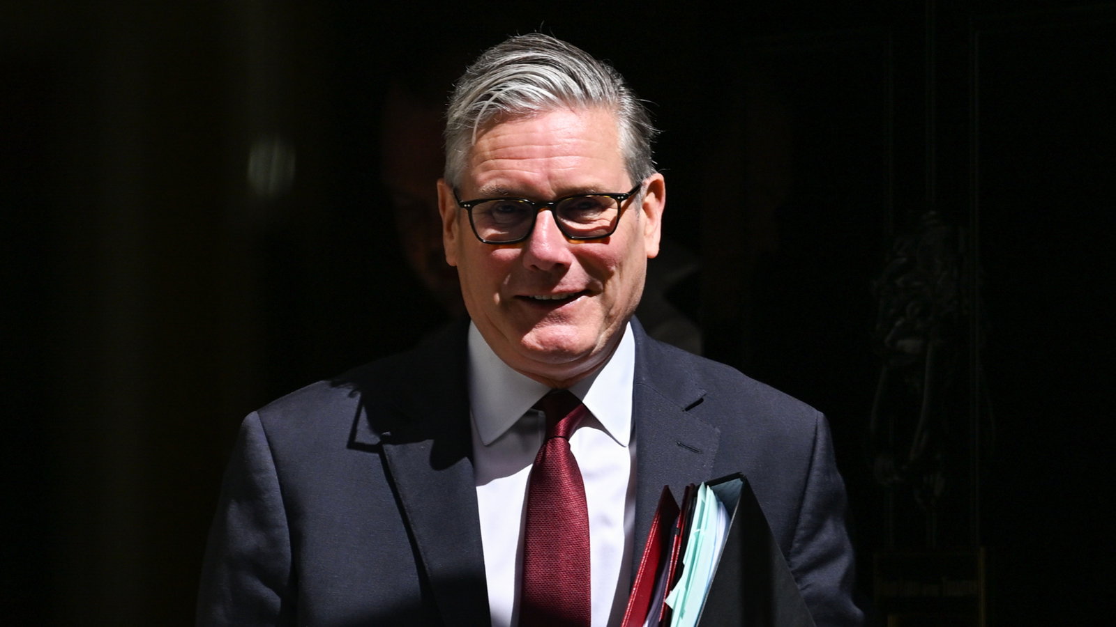Keir Starmer leaves Dowing Street wearing a dark suit, red tie and holding a black folder.
