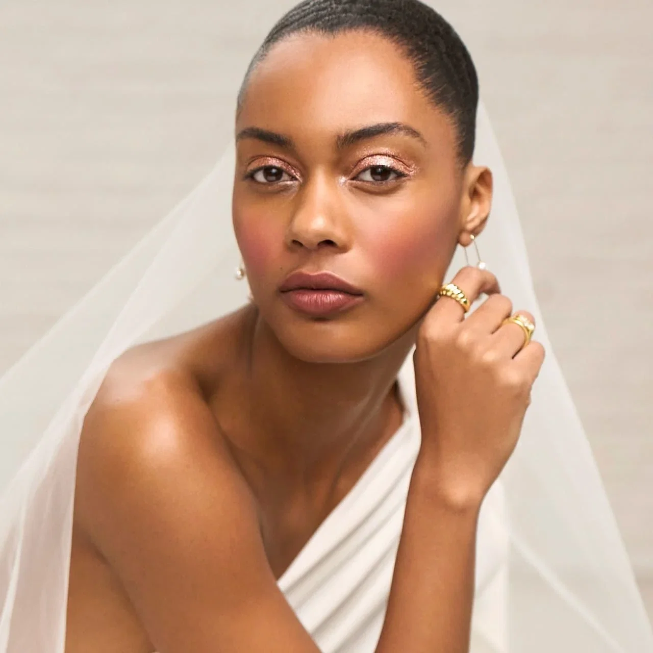 Woman wearing a wedding dress and veil with glowy makeup.