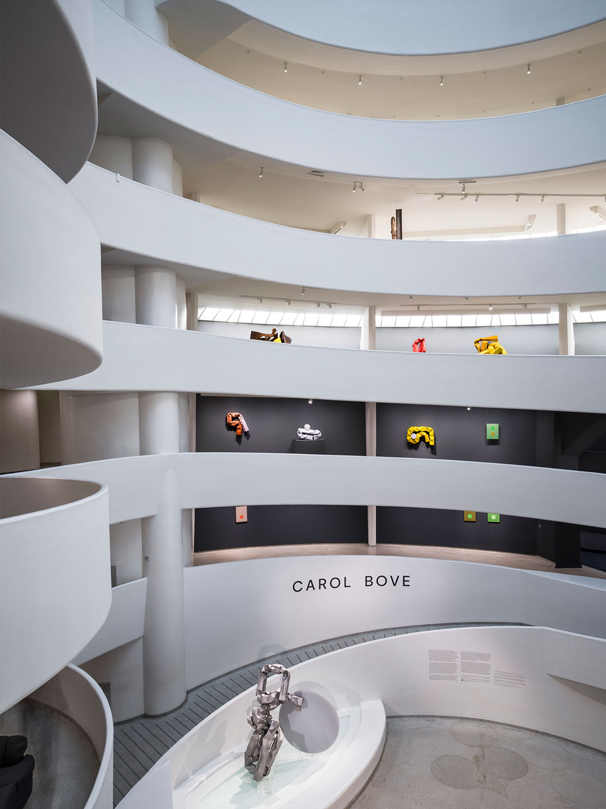 Interior of the Guggenheim Museum with visitors walking along the spiral ramps and viewing modern sculptures in the central atrium.