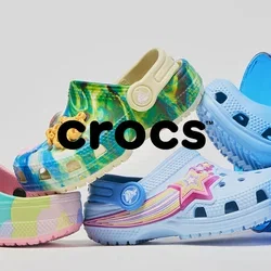 Vijf kleurrijke Crocs-schoenen speels in balans gerangschikt, waarvan twee in een omgevallen blauwe doorschijnende emmer op een witte achtergrond.