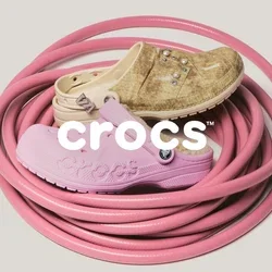 Opgerolde roze tuinslang met drie versleten rubberen schoenen in tan, beige en lichtroze erop gelegd tegen een effen achtergrond.