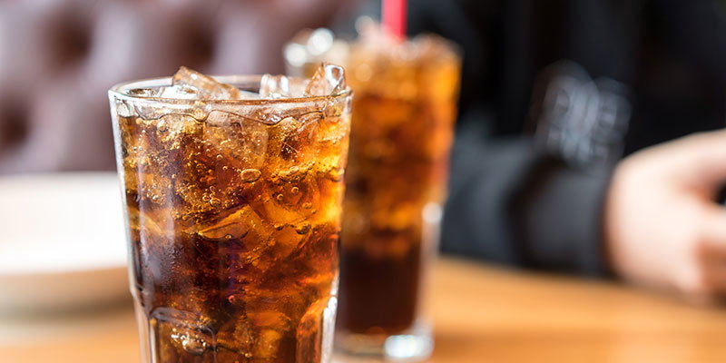 Two glasses of cola on a table.