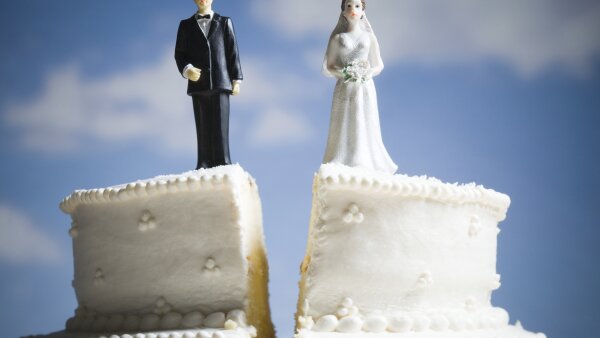 A wedding cake split in two with bride and groom toppers on the separated sections. 