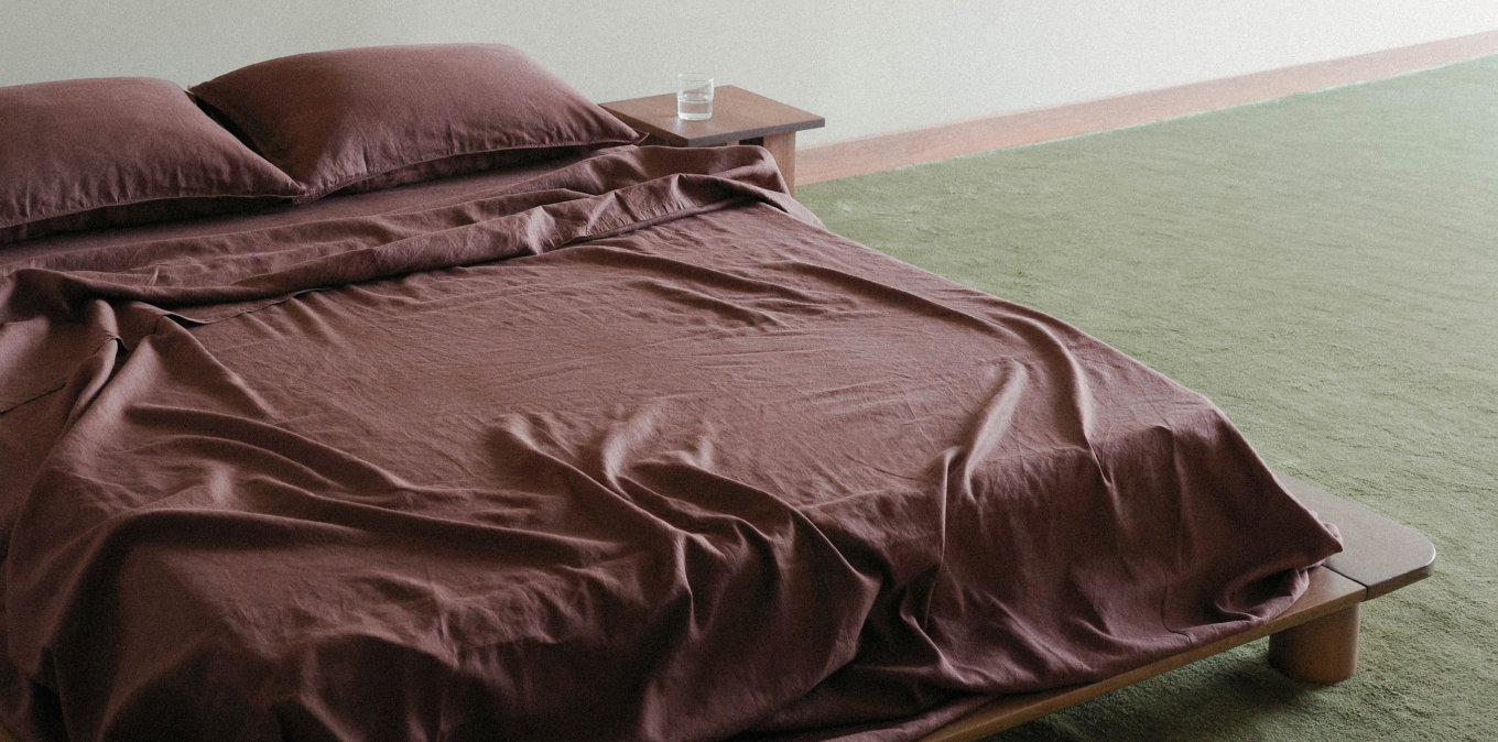 Dark purple sheets on a wooden bed frame with green carpet