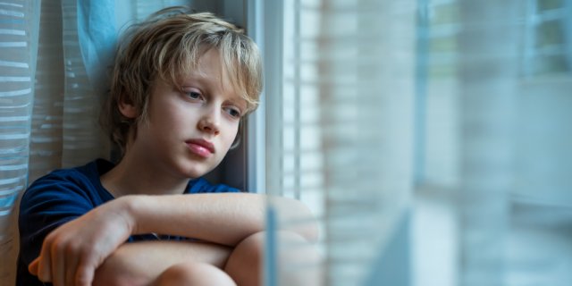 enfant triste qui regarde par la fenêtre