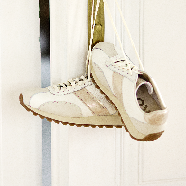 Pair of beige and white trainers hanging on a door handle