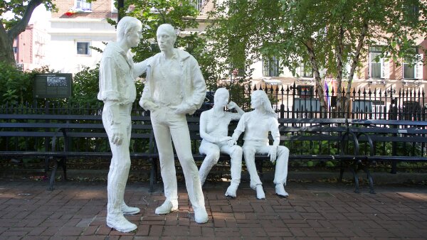 Stonewall National Monument in New York City. It features four white stone individuals. Two are sitting on a bench and two are standing in front of them.