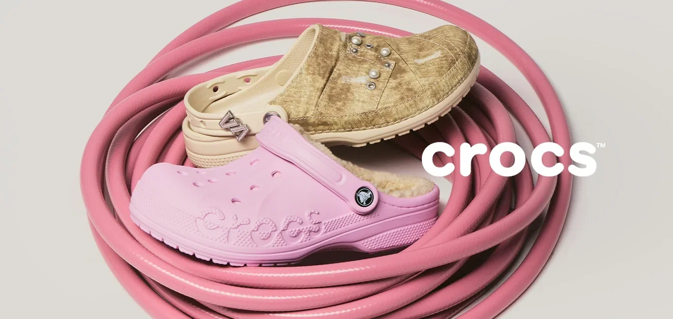 Opgerolde roze tuinslang met drie versleten rubberen schoenen in tan, beige en lichtroze erop geplaatst tegen een effen achtergrond.