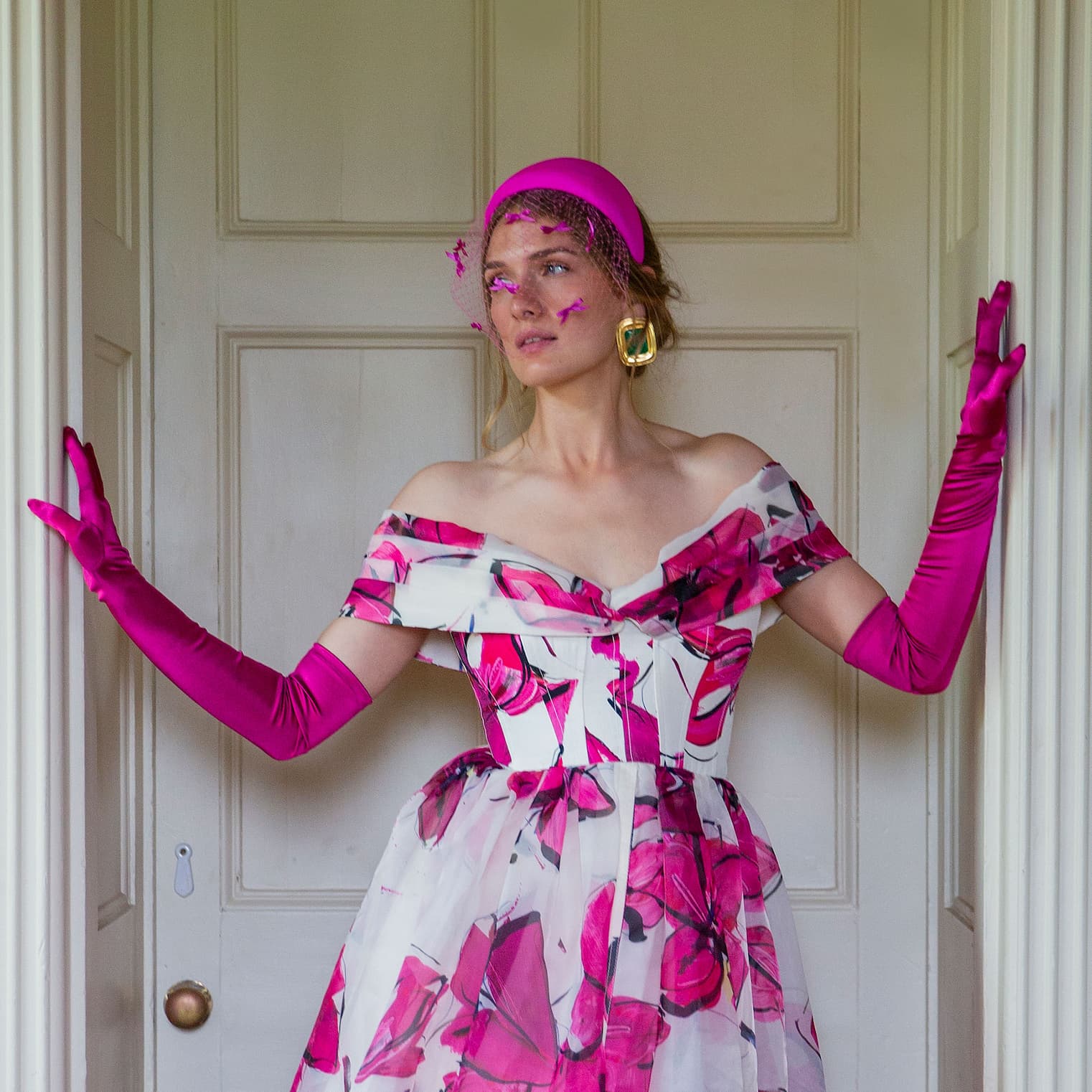 Woman wearing long opera satin gloves in pink, in a pink dress standing in the doorway. 