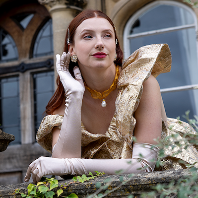 Woman wearing long opera satin gloves in champagne  while leaning on a balcony.