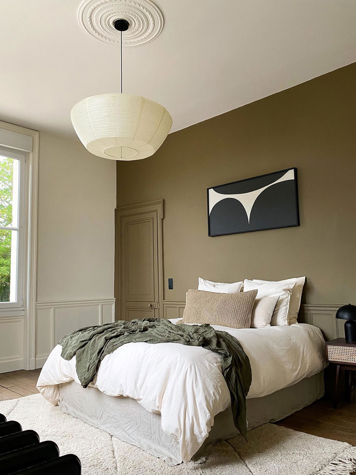 A cosy neutral bedroom with a striking olive green feature wall and colour drenched door. Classic panelling, white bedding, monochrome artwork and textured cushions add contrast and interest to this stylish space.