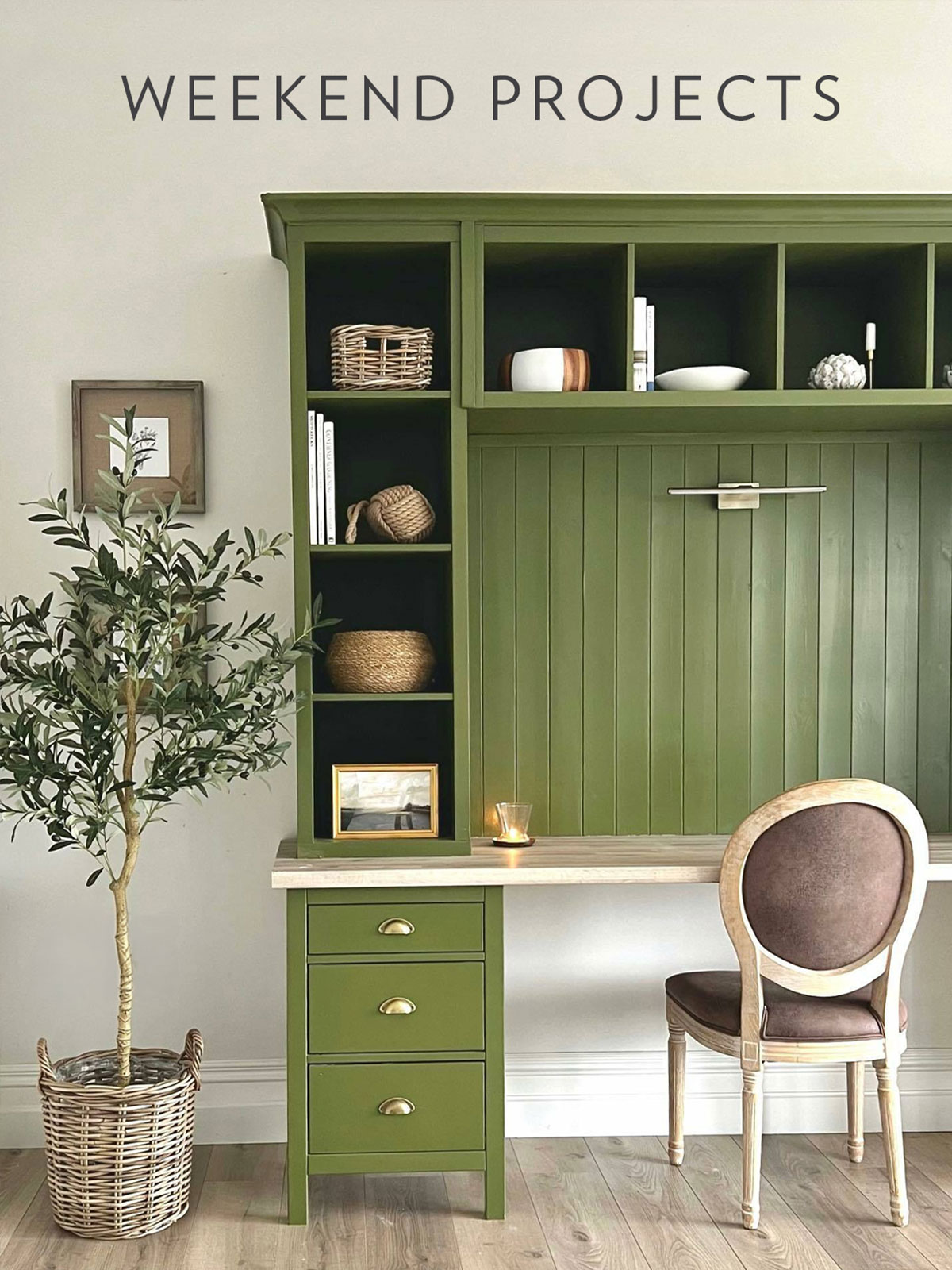 A tidy home office with green built‑in shelves, a wooden desk, a classic wooden chair, and a potted olive tree.