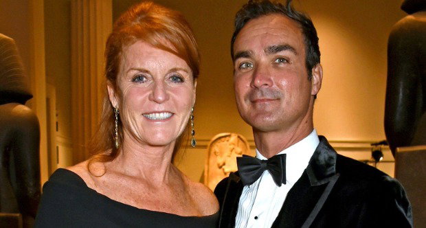 Sarah Ferguson in black dress with her hair up stands next to Manuel Fernandez who wears a black velvet jacket, white shirt and bow tie. They are both smiling at the camera.