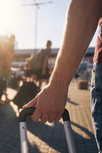 Traveller pulling a suitcase handle outside an airport.