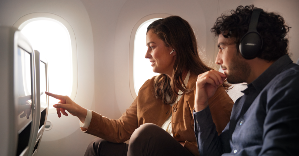 Two passengers on an airplane looking at a screen together.