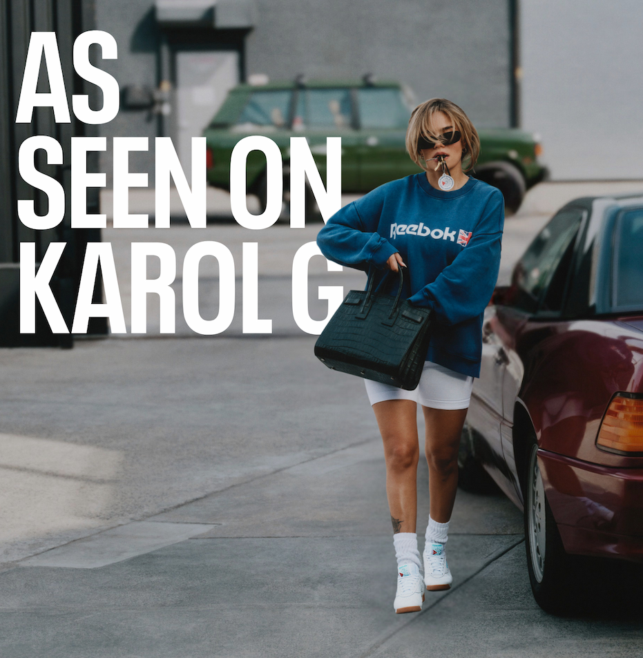 Karol G wearing the Freestyle Lo and an oversized Reebok sweatshirt walks outdoors carrying a handbag. Text reads: “AS SEEN ON KAROL G.”