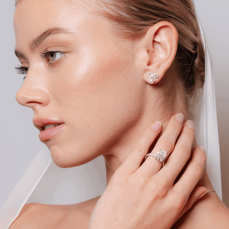 Woman wearing a veil, pearl earring and diamond engagement ring. The new edit. Discover new wedding jewelry. Click shop now.