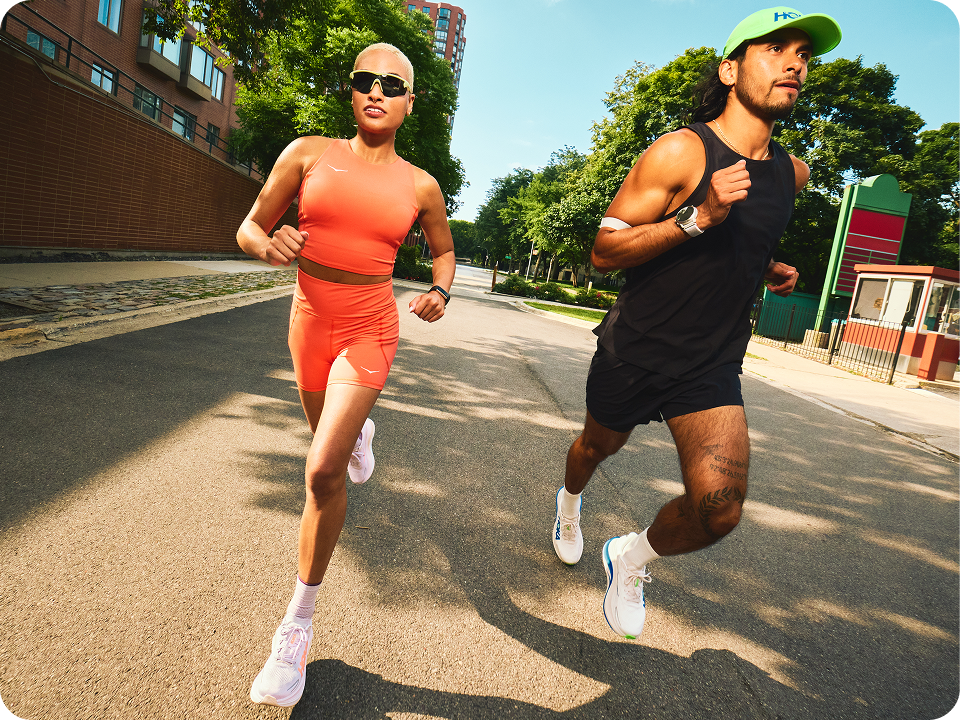 An image of two people running on an empty street with buildings and trees in the background.