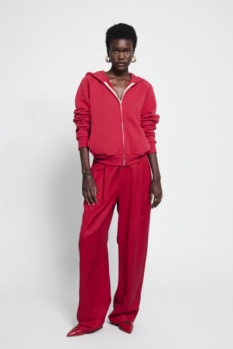 Woman in red zip-up hoodie and wide-leg pants stands against a white background.