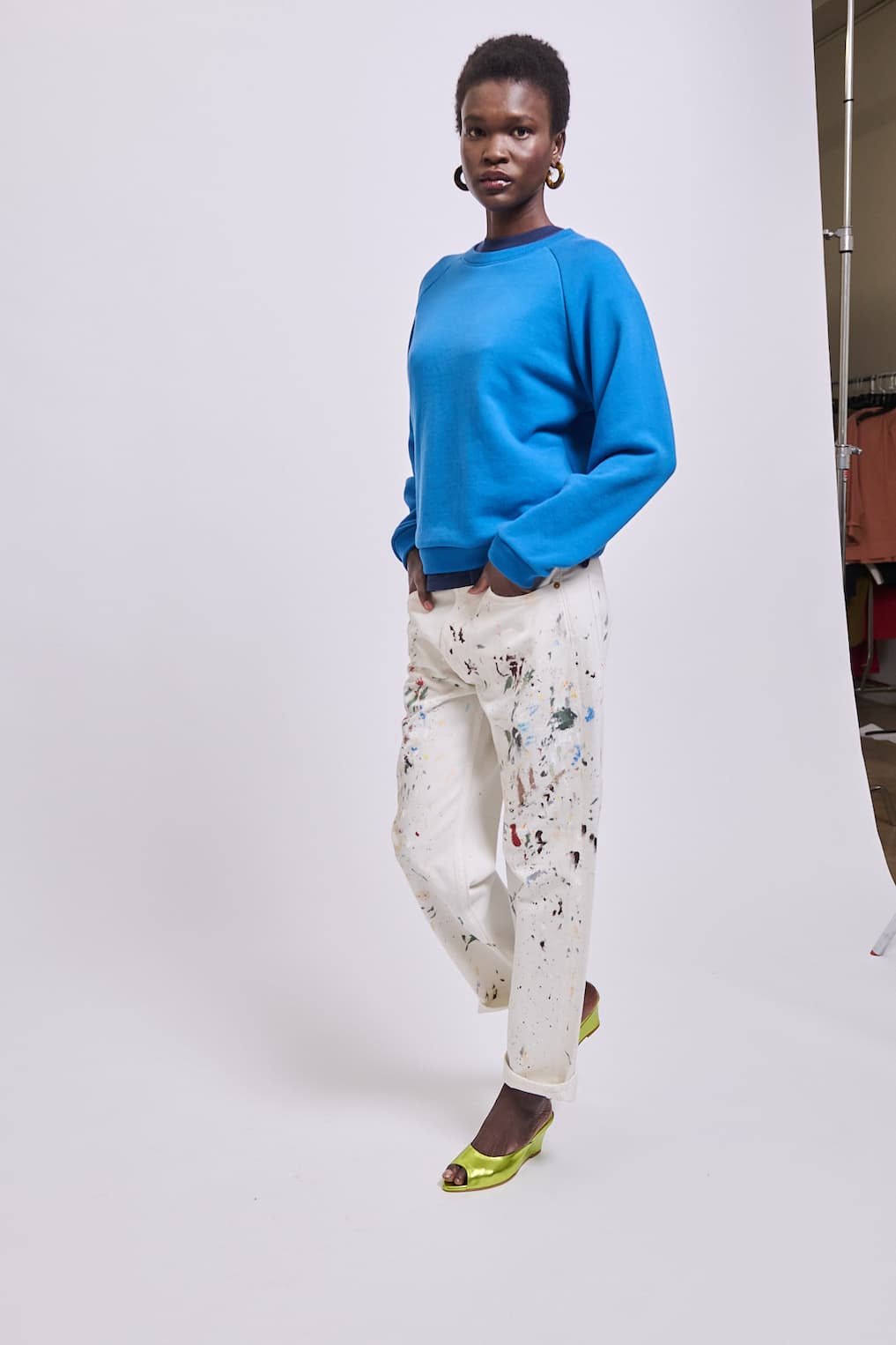 A person wearing a tan hoodie and dark pants sits with their hand on their head.