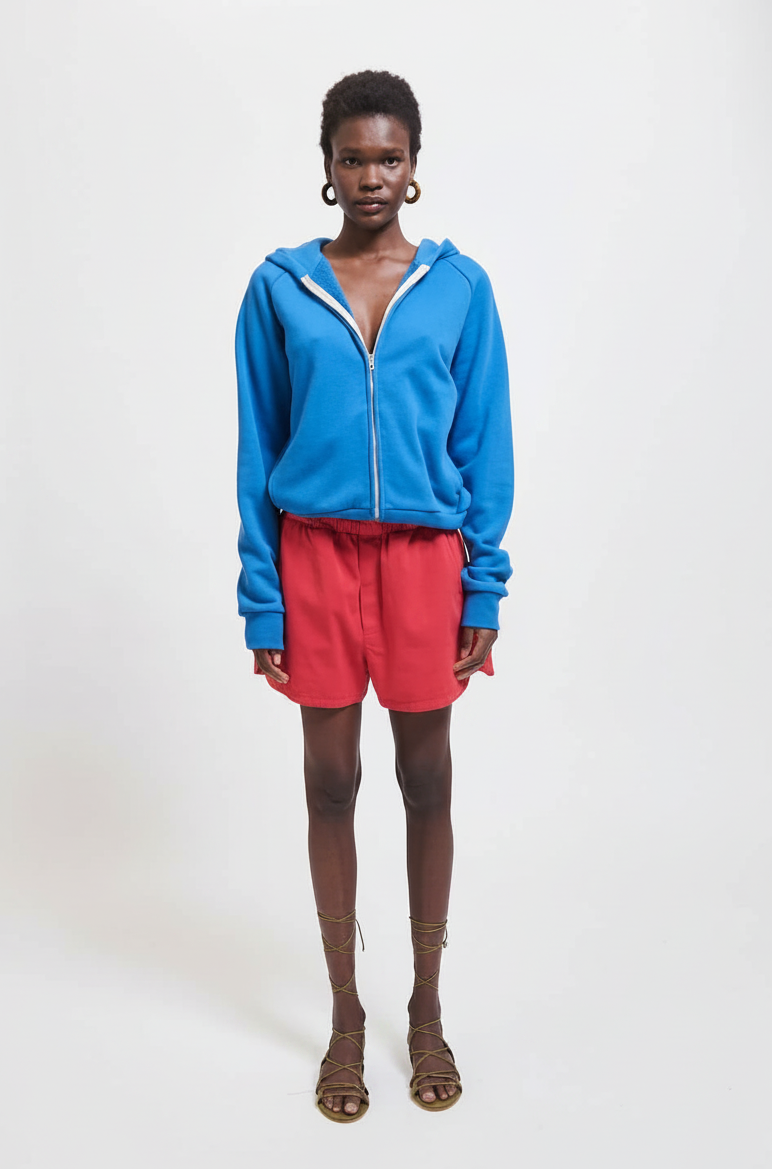 Woman in blue zip-up hoodie and red shorts stands facing forward.