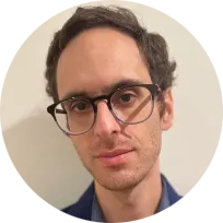 Josh, a thin, balding  white man with a thick brown beard, wears a neutral expression, and a blue dress shirt.
