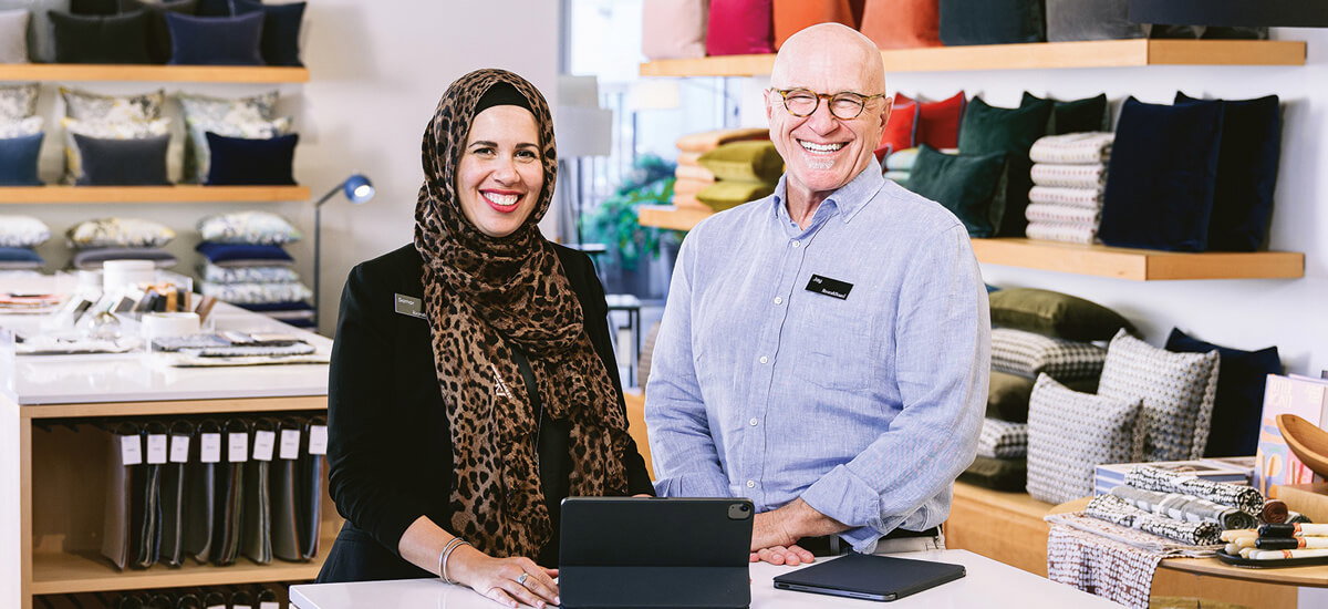 Design associate smiling while working at a computer in a showroom with colorful pillows on display.