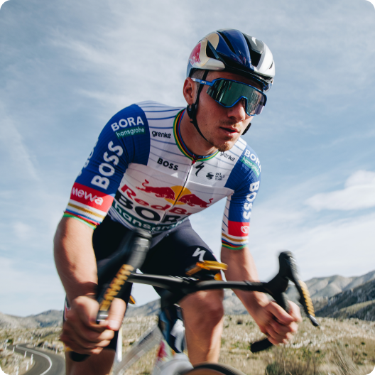 Professional cyclist in blue team kit and helmet riding a road bike on a mountain road, leaning forward and wearing reflective sunglasses
