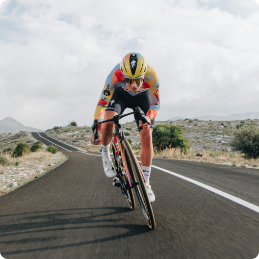 Competitive cyclist in aerodynamic position on road bike wearing yellow helmet and colourful kit, racing on a winding mountain road