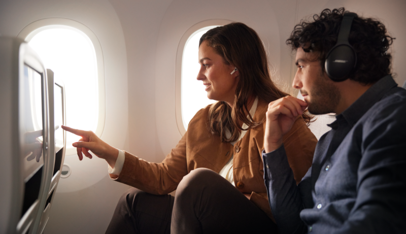 Due passeggeri in aereo guardano uno schermo insieme.