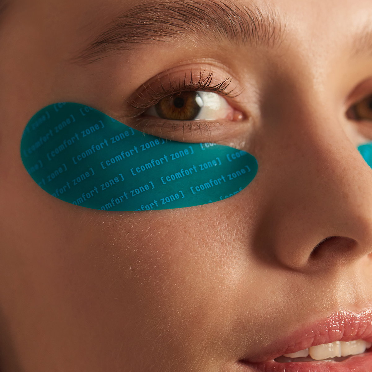 Close up of woman's eyes. She's wearing blue eye patches that say Comfort Zone