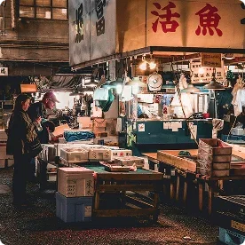 People browsing a bustling, traditional indoor fish market with boxes of seafood and Mandarin signage.