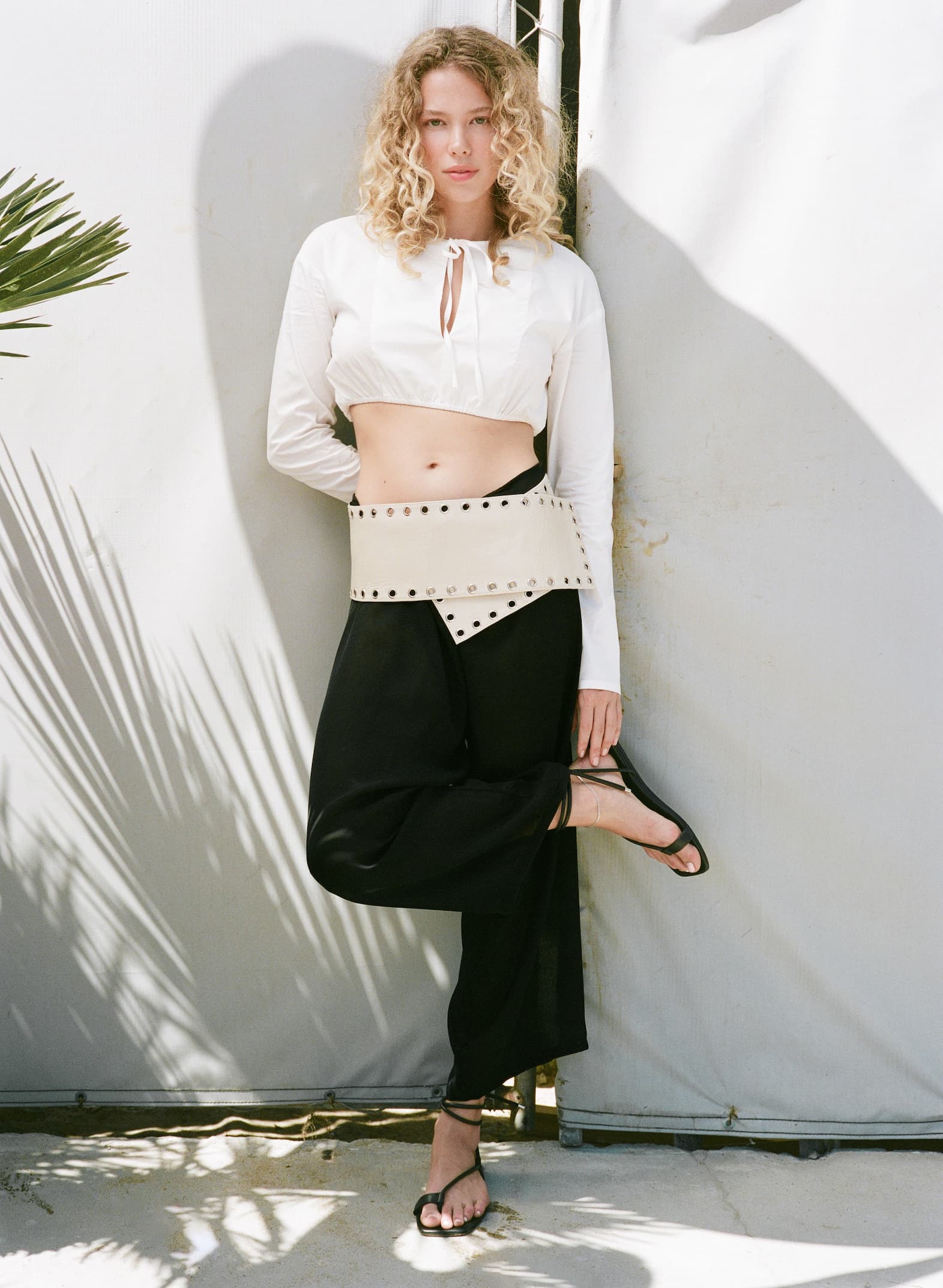Woman standing against wall, holding heel of foot with black strappy sandals