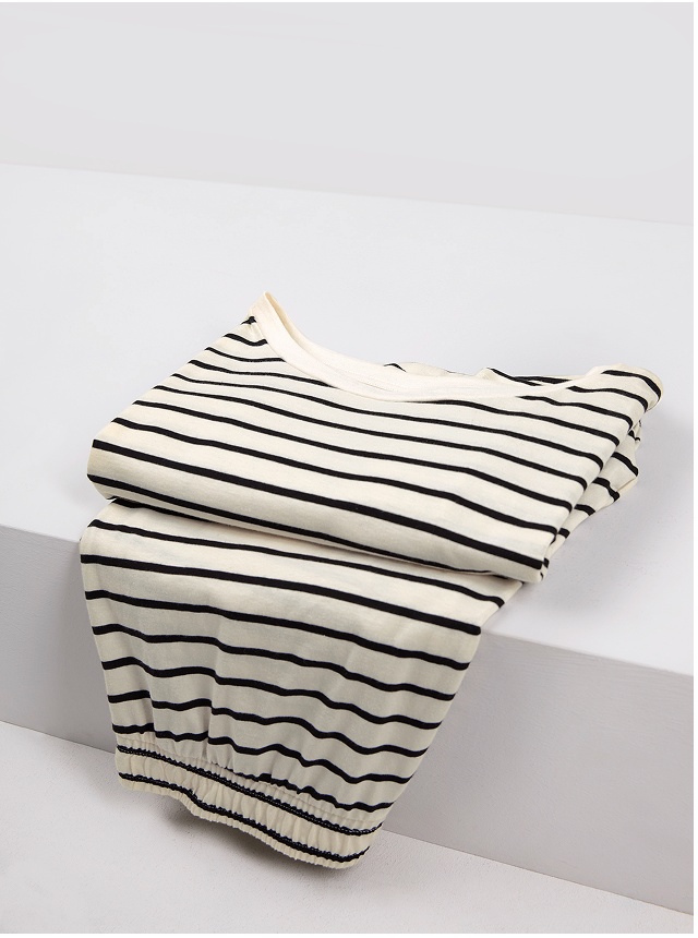 The model is wearing a striped short-sleeved shirt and striped shorts, both in the color “Charm Cream” and from the FAVOURITES LAYERING collection by CALIDA.