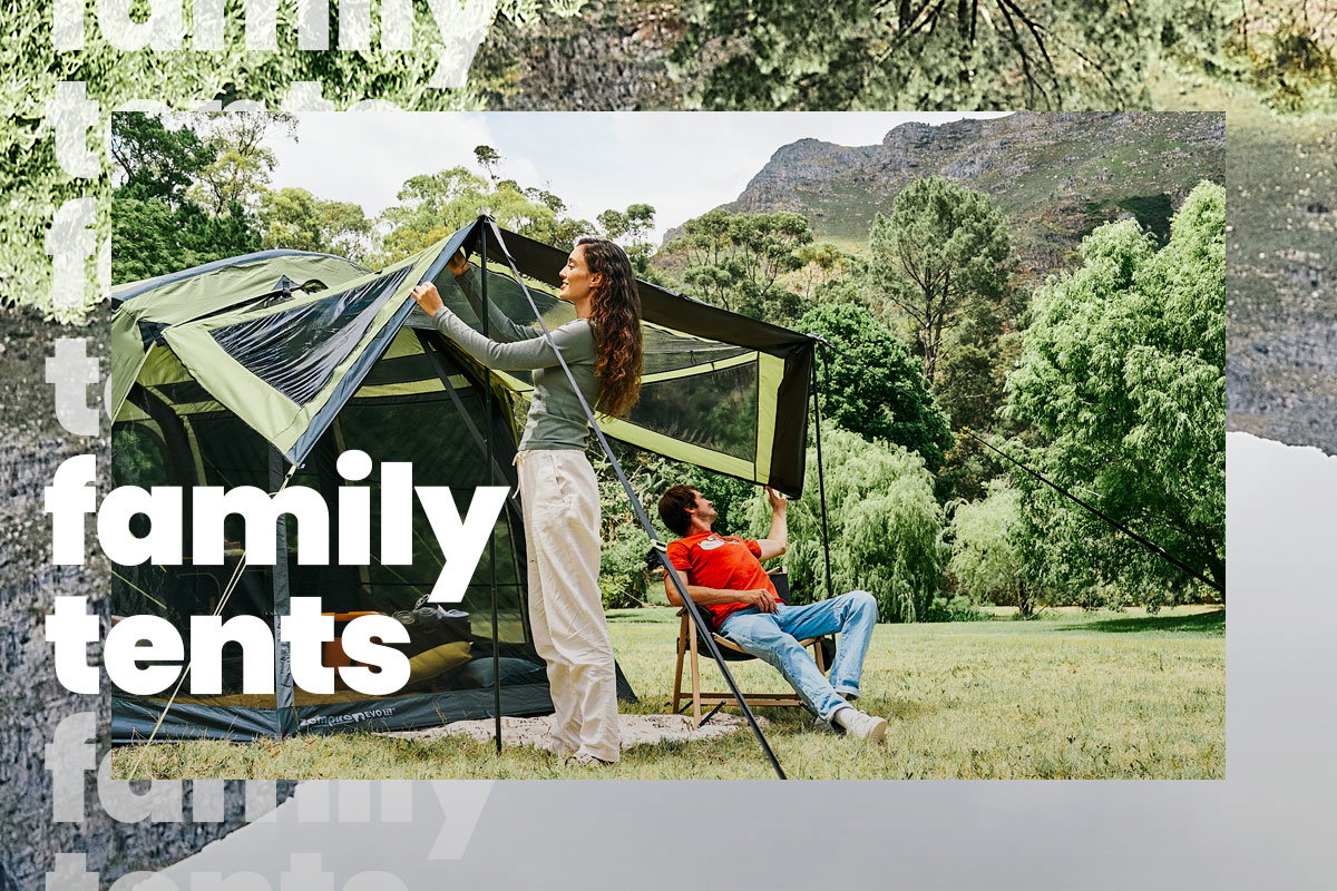 Two people setting up their tent in a field surrounded by trees and mountains