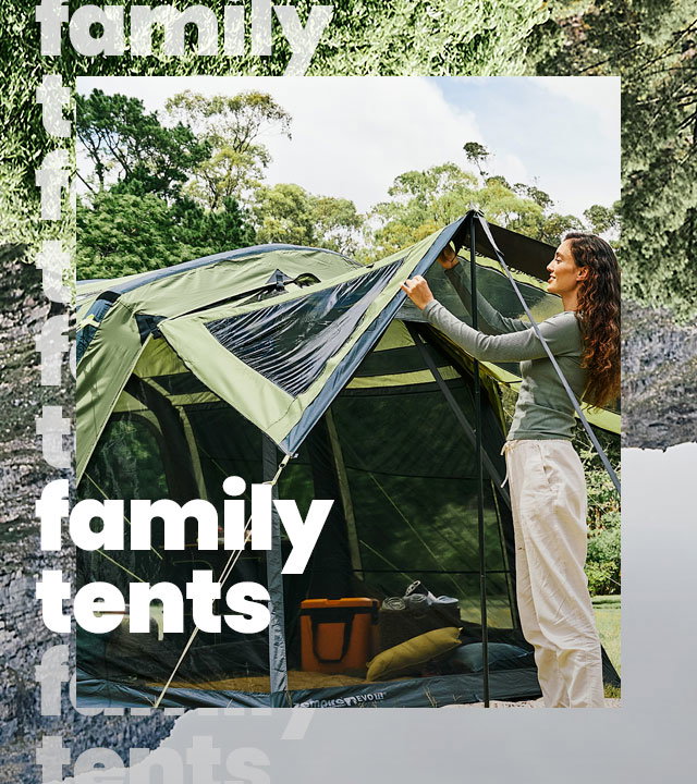 Two people setting up their tent in a field surrounded by trees and mountains