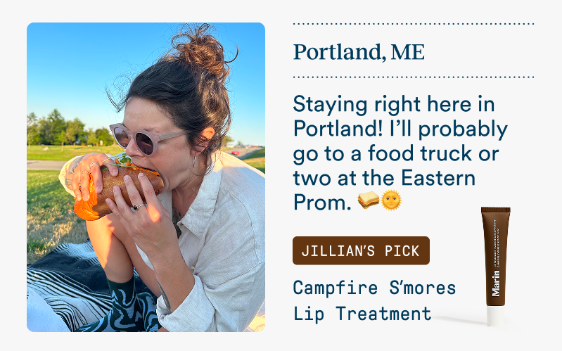 A woman wearing sunglasses enjoys a sandwich picnic outdoors in Portland, Maine during golden hour. Text mentions visiting food trucks at the Eastern Prom. Featured product: Campfire S’mores Lip Treatment.