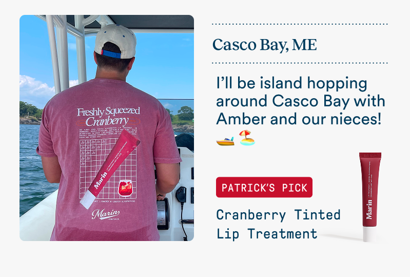 A man stands on a boat in Casco Bay, Maine wearing a cranberry-colored Marin graphic tee featuring Cranberry Lip Treatment artwork on the back. Text says he’ll be island hopping with Amber and their nieces. Featured product: Cranberry Tinted Lip Treatment.