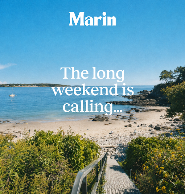 A sunny coastal Maine beach scene with rocky shoreline, blue ocean water, and greenery framing a staircase path down to the beach. White text reads “The long weekend is calling…” with the Marin logo above.