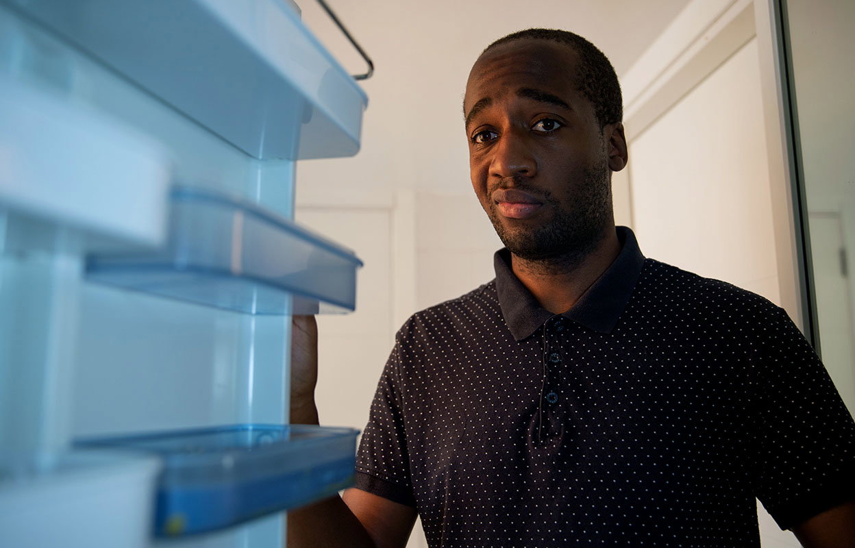A man looking into his fridge with a perplexed expression