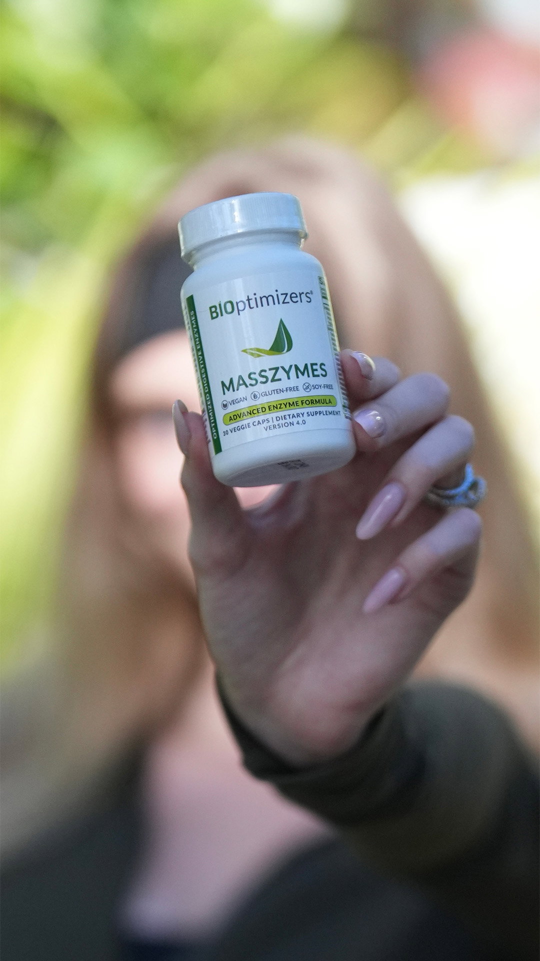 a woman holding a bottle of BIOptimizers Masszymes towards camera