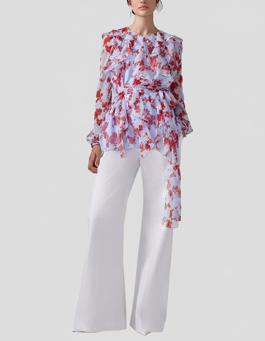 Woman in a floral print ruffled blouse and white wide-leg pants.