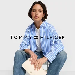 Blauw-wit gestreepte blouse met lange mouwen, witte t-shirt, lichtblauwe jeans en witte sneakers. Houdt een crèmekleurige clutch met een logo vast.