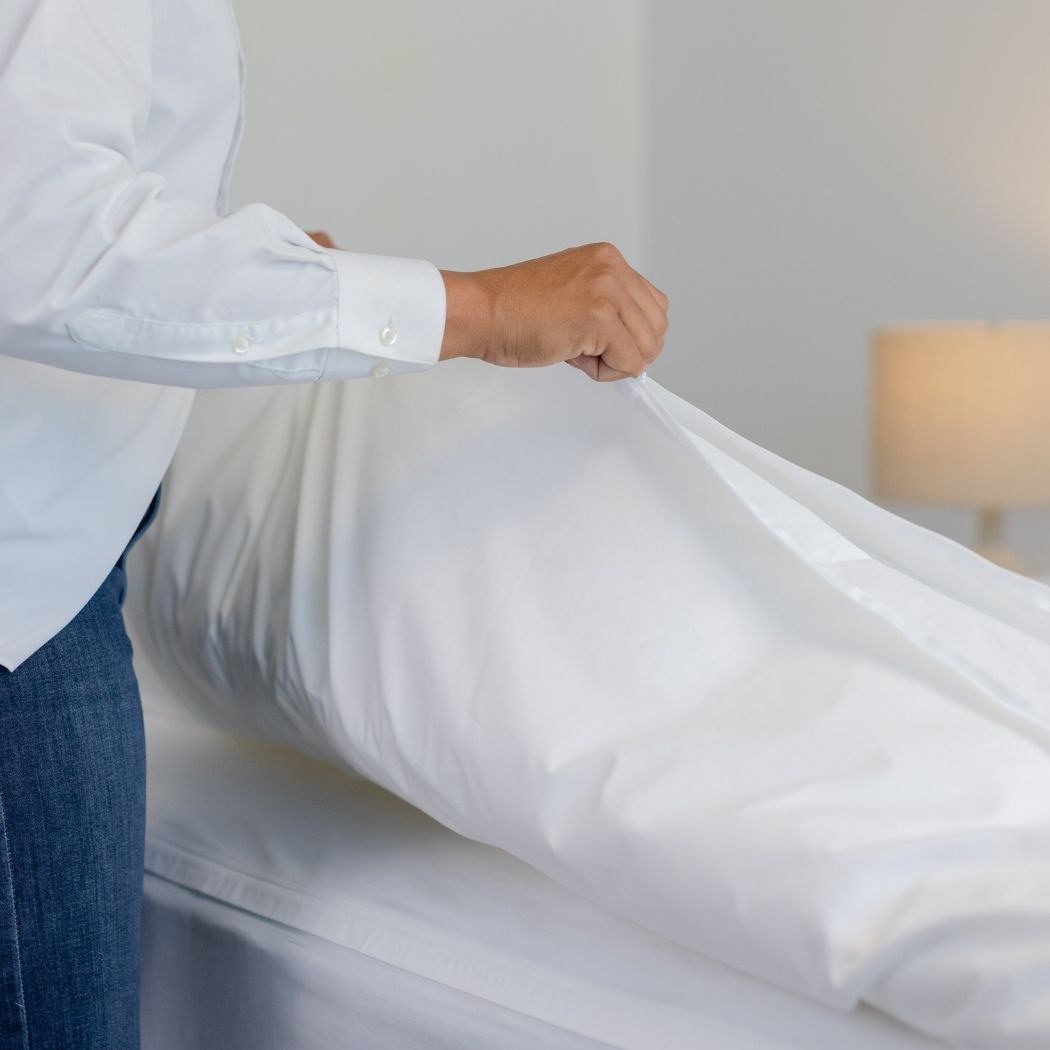 A woman zips a white duvet cover onto her bed